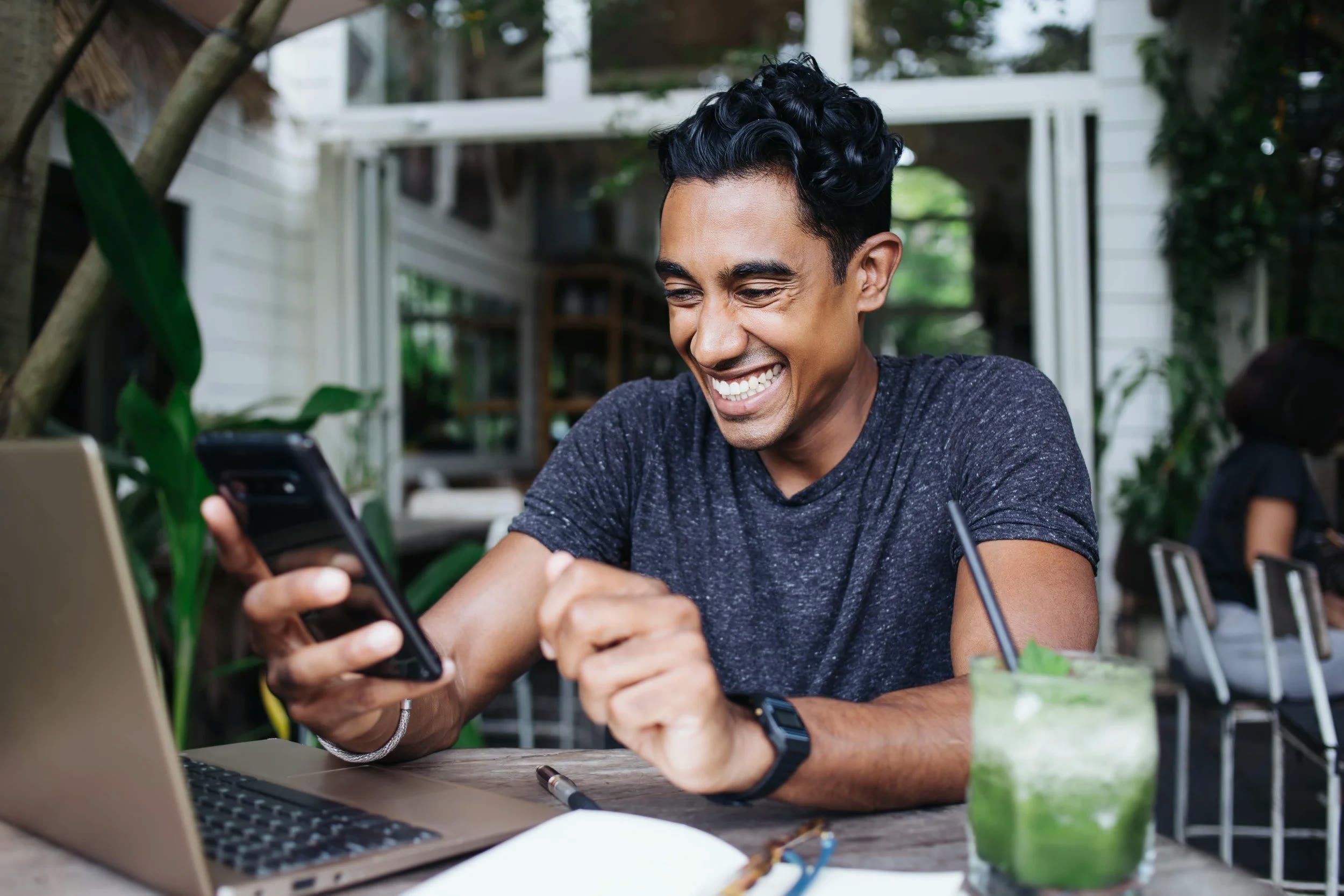 A smiling customer checking a phone at an outdoor cafe table